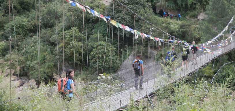 Trekkers crossing river through suspension bridge